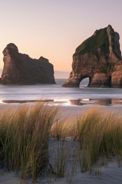 Wharariki Beach is a wild, windswept stretch of sand framed by towering rock arches and rolling dunes.