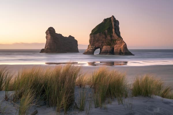 Wharariki Beach is a wild, windswept stretch of sand framed by towering rock arches and rolling dunes.