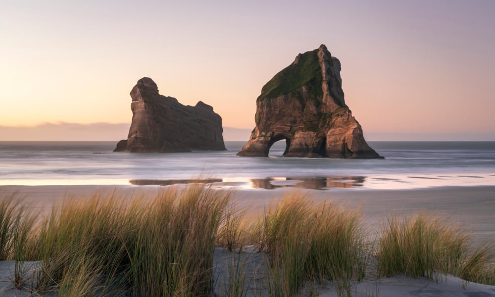 Wharariki Beach is a wild, windswept stretch of sand framed by towering rock arches and rolling dunes.